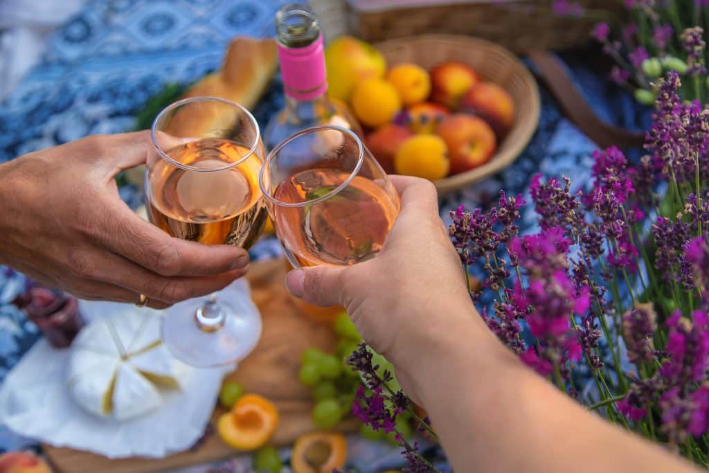 Two glasses of rosé wine being toasted over a picnic with bread, fruit and lavender